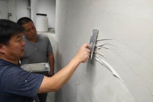 A site technician examining wall putty rolling under a steel trowel on a real jobsite wall