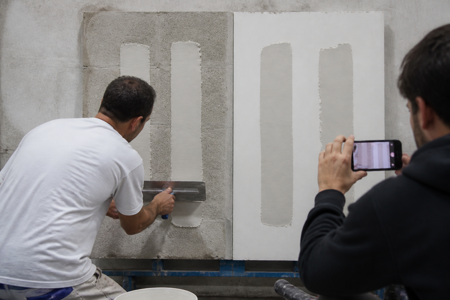 A technician using a steel trowel across adjacent wall putty panels on absorbent and sealed substrates