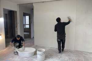 Wide view of workers applying white gypsum plaster on an interior construction wall